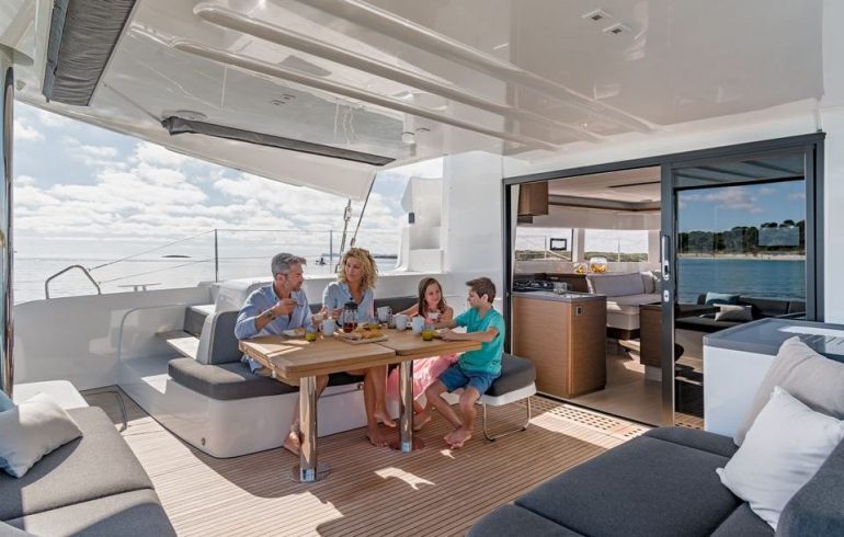 Lagoon 50 aft deck features dinning table, sun mattresses and hard bimini top